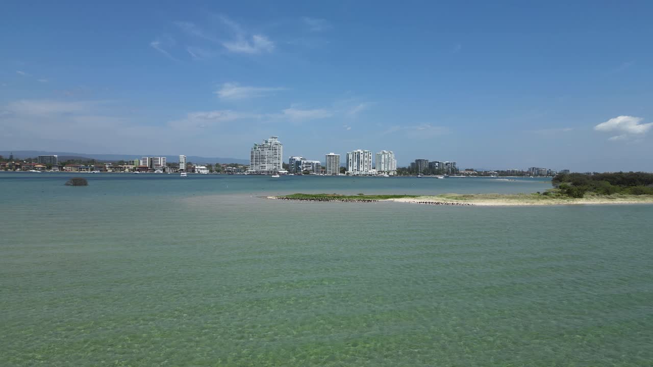 una bandada de aves marinas migratorias descansa en una isla de arena natural cerca del horizonte de una ciudad urbana