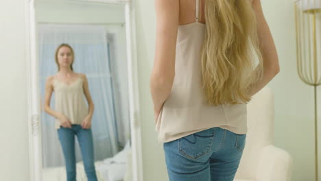 vista trasera de una mujer flaca mirando su vientre levantándose la camisa frente al espejo