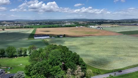 aerial wide shot of agricultural farm fields and cars on street during beautiful weather in america. green trees farmsteads and shadow of clouds on field.