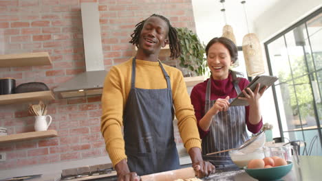 pareja feliz en delantales usando tableta y hornear en la cocina, espacio de copia, cámara lenta