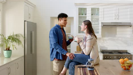 Happy-diverse-couple-talking-and-drinking-coffee-in-kitchen-at-home,-in-slow-motion