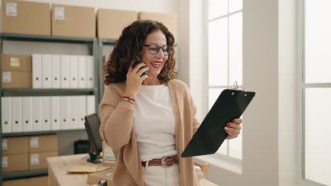 middle age woman ecommerce business worker talking on the smartphone reading document at office