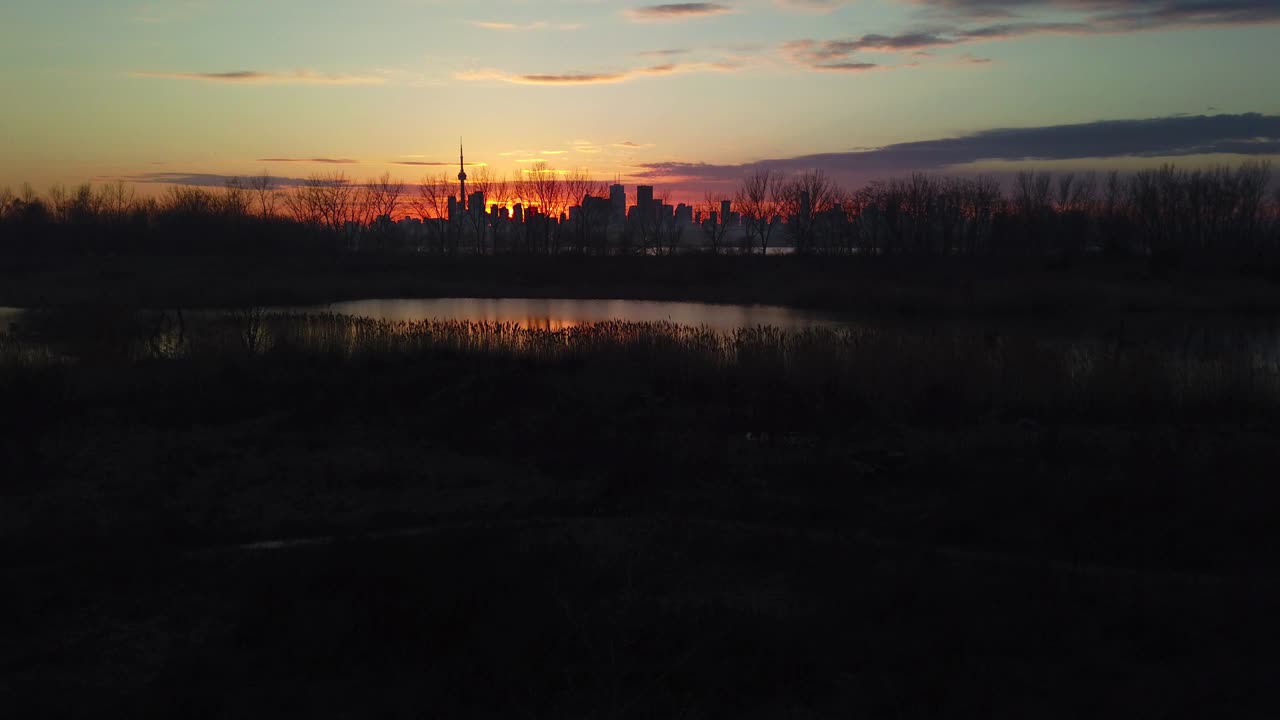 Slow magic hour pan of serene wetlands with city skyline in the distance