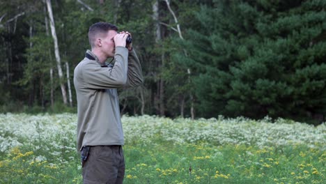 side view of caucasian man in the grassland with wildflowers looking far through binoculars