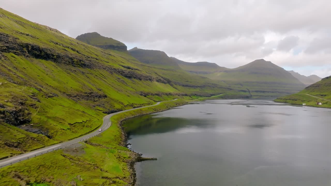A calm Faroe landscape with winding road, green mountains, and serene water views