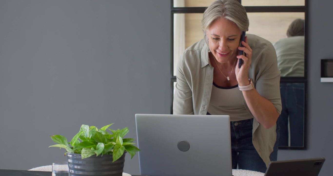 Ricevendo una telefonata, donna di mezza età che tiene il telefono, controlla il laptop e si guarda allo specchio durante una chiamata di lavoro.