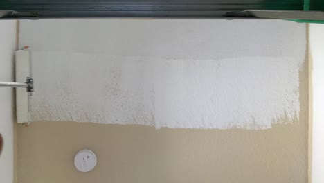 hands of a man painting ceiling white with paint roller inside house