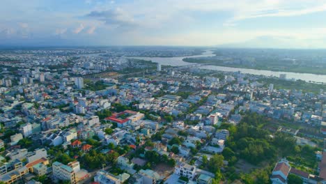 Vista-Aérea-Del-Paisaje-Urbano-Plano-De-La-Ciudad-Vietnamita-Y-El-Río-Durante-La-Puesta-De-Sol