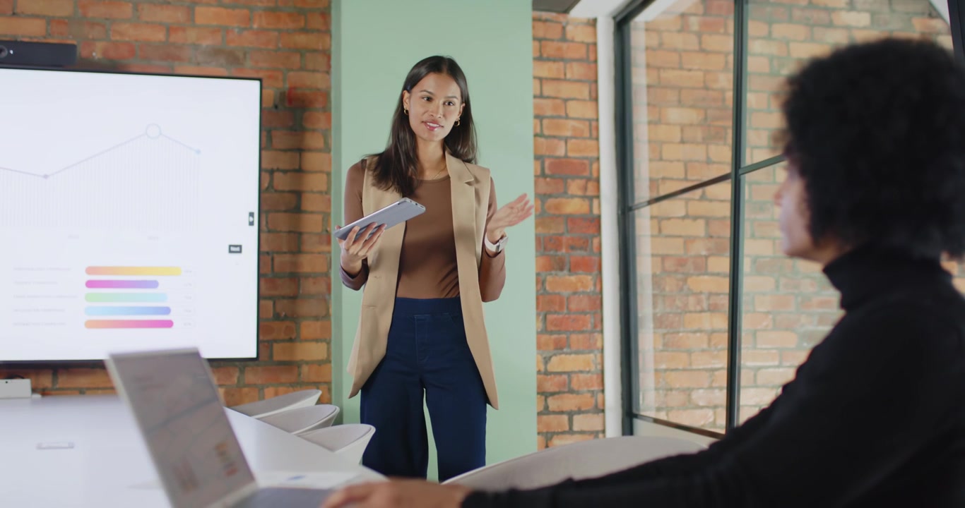 African American presenter in blazer holding tablet, gesturing, explaining chart to peer in meeting
