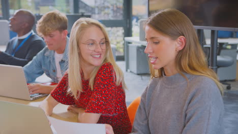 university or college students sitting around table with tutor collaborating in seminar on laptop