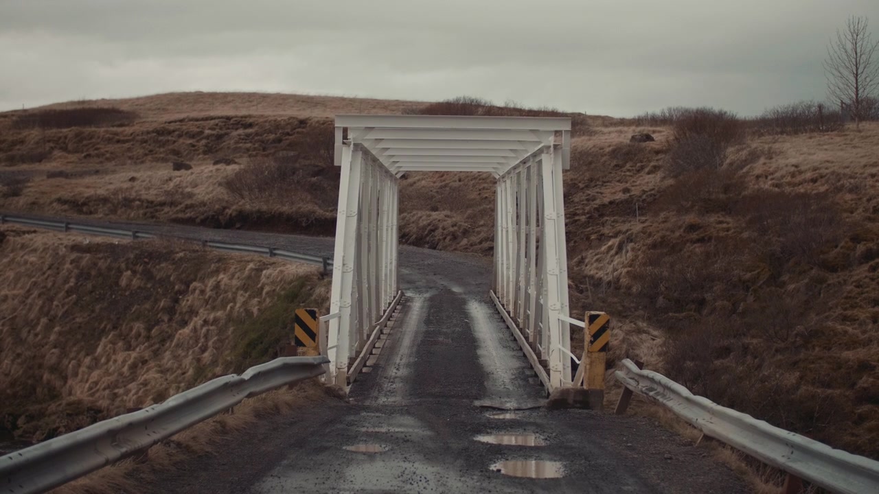 Rural Dirt Road Leading to a White Metal Bridge on Overcast Day