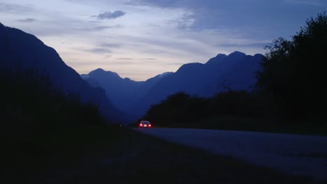 car drives towards silhouetted mountains at twilight