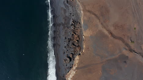 Top-down-flying-towards-amazing-black-beach-in-Iceland.-Overhead-birds-eye-of-spectacular-coastline-with-rocks-and-black-volcanic-sand