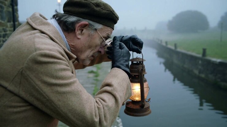 Glancing at canal, senior man coat, cap adjusting specs, moving lantern, checking water, copy space