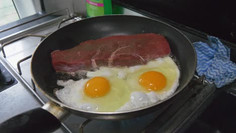 bistec crudo y huevos cocinando en una sartén en una autocaravana o campervan