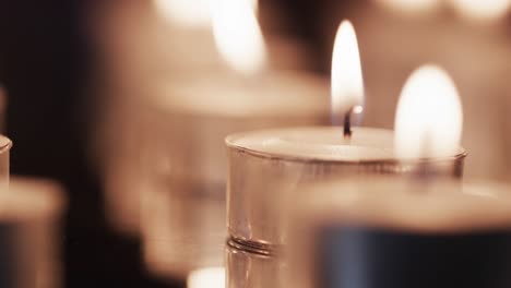 Video-of-close-up-of-rows-of-tea-candles-with-white-flames-and-copy-space-on-black-background