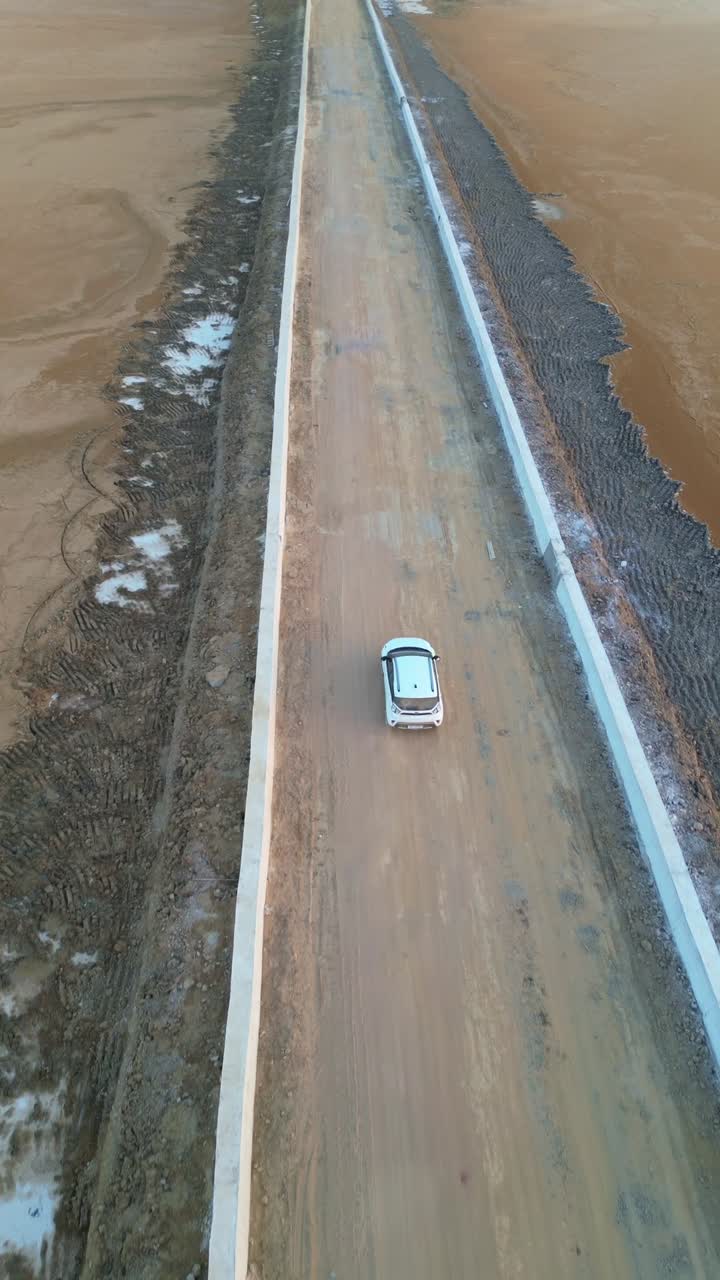 A forward-moving aerial view shows a car driving on a straight road in Kutch, Gujarat, India, surrounded by endless golden sand dunes 4K