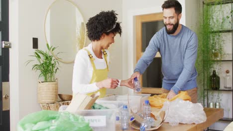 Video-of-happy-diverse-couple-having-fun-sorting-recycling-at-home,-with-copy-space