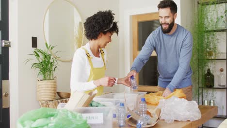video de una feliz pareja diversa divirtiéndose clasificando el reciclaje en casa, con espacio para copiar