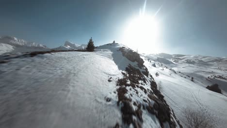 Vista-Aérea-Con-Drone-Fpv-De-Una-Montaña-Nevada-Hacia-El-Sol