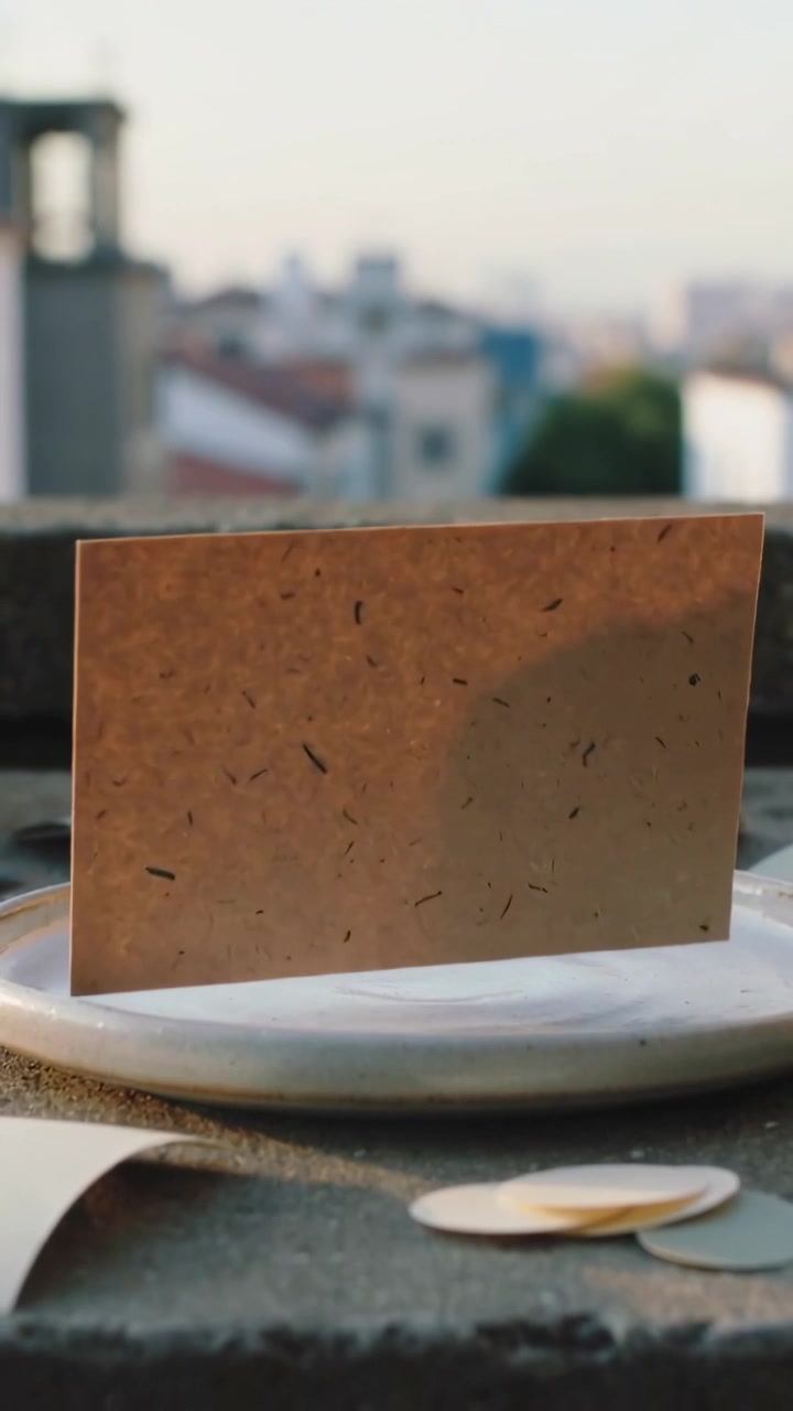 Vertical video: Lifting handmade paper above plate on parapet by mild breeze, rotating near tokens