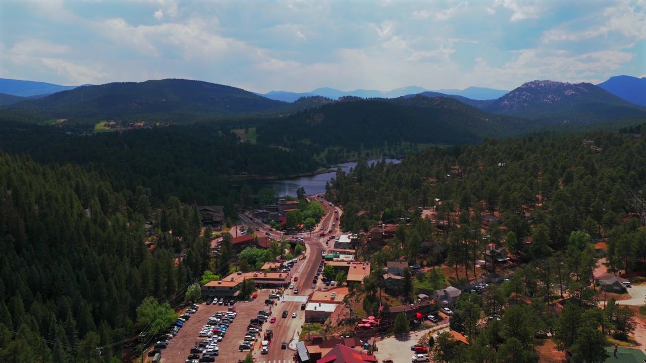 Vista aerea con drone del centro di Evergreen, Colorado, con la via principale, edifici commerciali, auto e il Lago Evergreen. Si vedono anche il Campo da golf di Denver, il Monte Blue Sky e il Front Range delle Montagne Rocciose. Mattina di primavera/estate, soleggiata e nuvolosa, con movimento all'indietro.