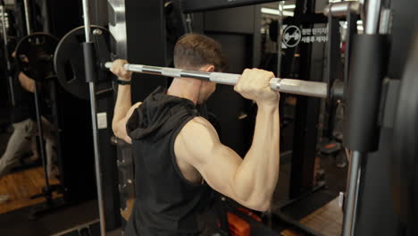 strong muscular adult man doing shoulder press in smith machine at gym - close-up