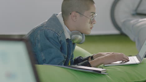 young mixed race man student using digital laptop computer working on project browsing online research planning strategy relaxing in colorful modern office wearing glasses