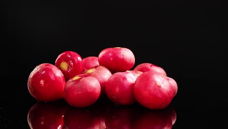 a group of radishes rotates smoothly on a glossy black surface, highlighting their vibrant color and texture