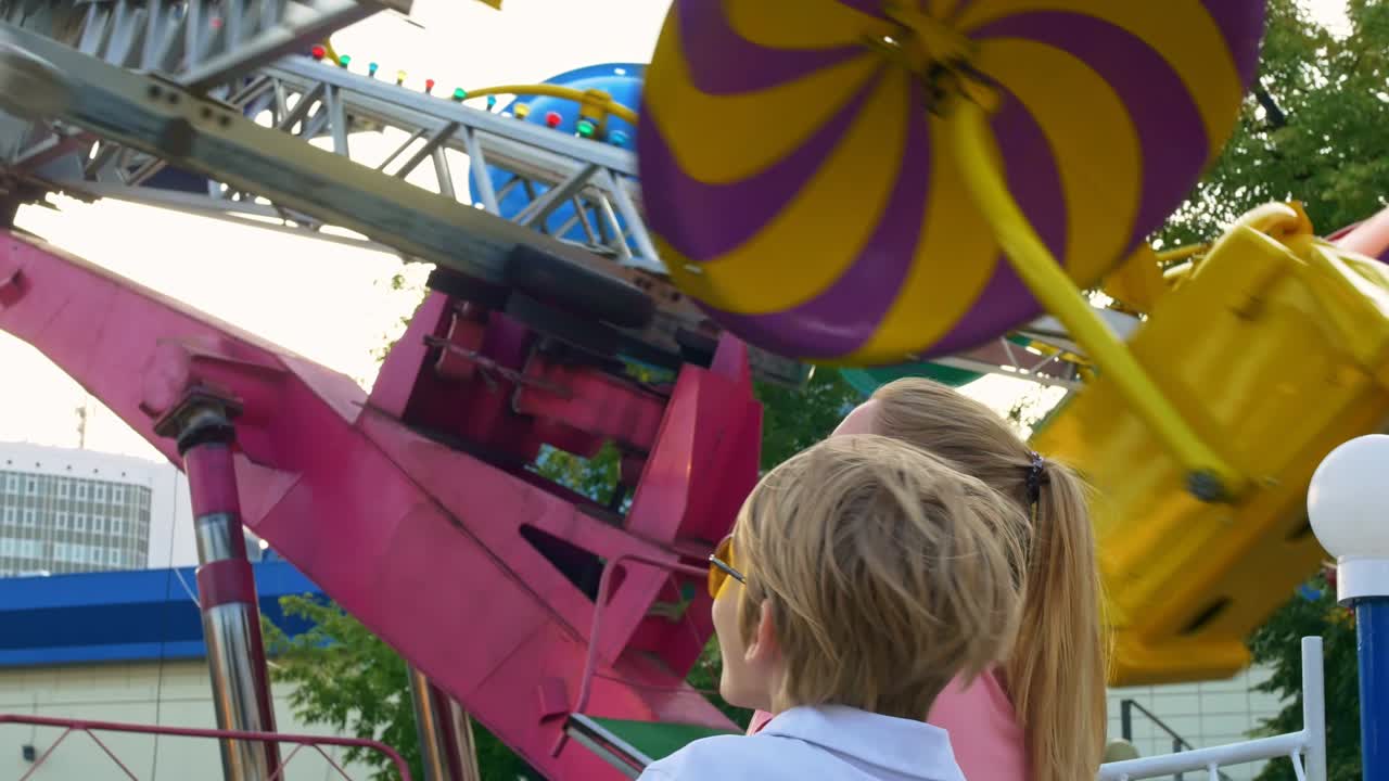 madre e hijos se paran en el carrusel giratorio en el parque de atracciones, divirtiéndose y decidiendo montar en este carrusel rápido y emocionante. diviértete en la feria del domingo