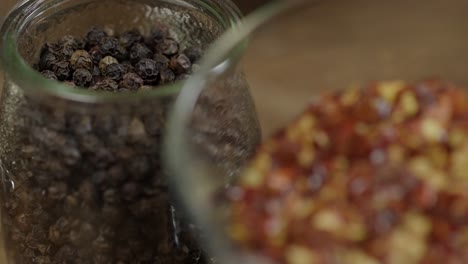 closeup view of jars containing spices for chimichurri sauce, black pepper and dried red chili