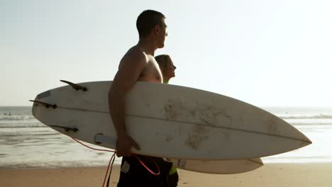 couple holding boards and walking on beach