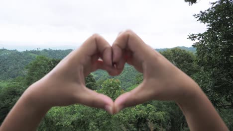 small hands forming a heart shape framing the trees in the mountain range