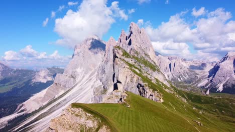 aerial view with parallax of the peaks of seceda with green pastures, and hiking trails in the foreground, and mountain peaks in the background in the italian dolomites in south tyrol, italy