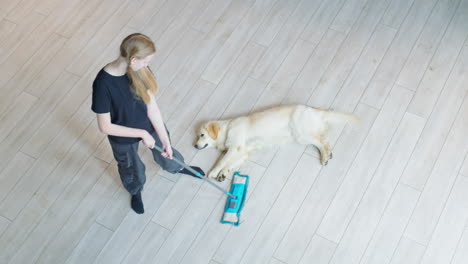 teenage girl cleaning the floor with a mop while a dog is resting on the floor