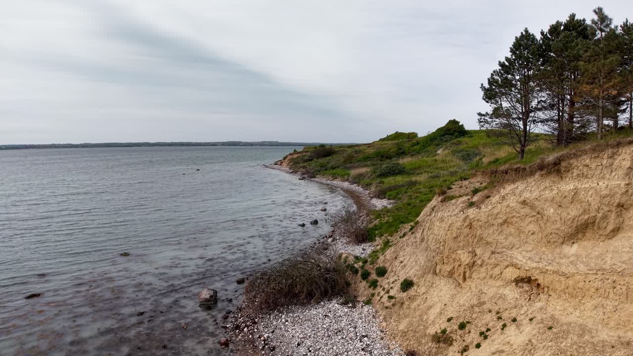 Drone view along an eroding coastline where cliffs meet the sea under an overcast sky