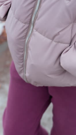 primer plano de la parte inferior del cuerpo con pantalones marrones y botas negras caminando por un camino de invierno áspero cubierto de follaje esparcido y manchas heladas, nieve y mezcla de tierra en el suelo desigual