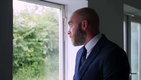 a sad pensive lonely businessman looking up at a grey sky and rain outside of his office window