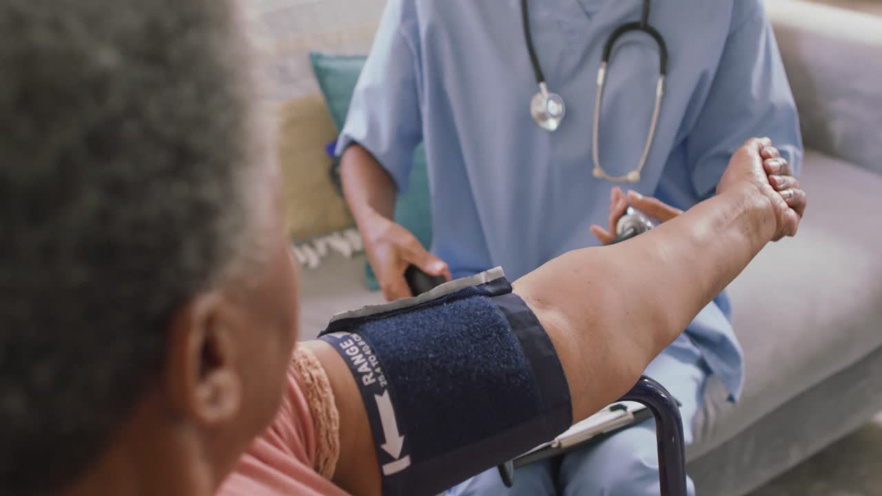 African american female doctor checking blood pressure of african american senior woman at home