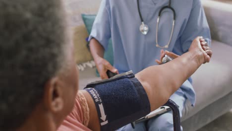 african american female doctor checking blood pressure of african american senior woman at home