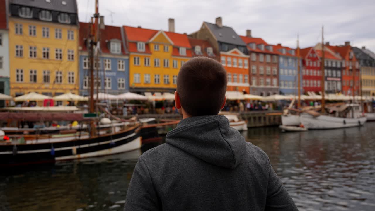 Man arranges his clothes while enjoying colorful buildings and boats of Nyhavn waterfront