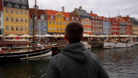 man arranges his clothes while enjoying colorful buildings and boats of nyhavn waterfront