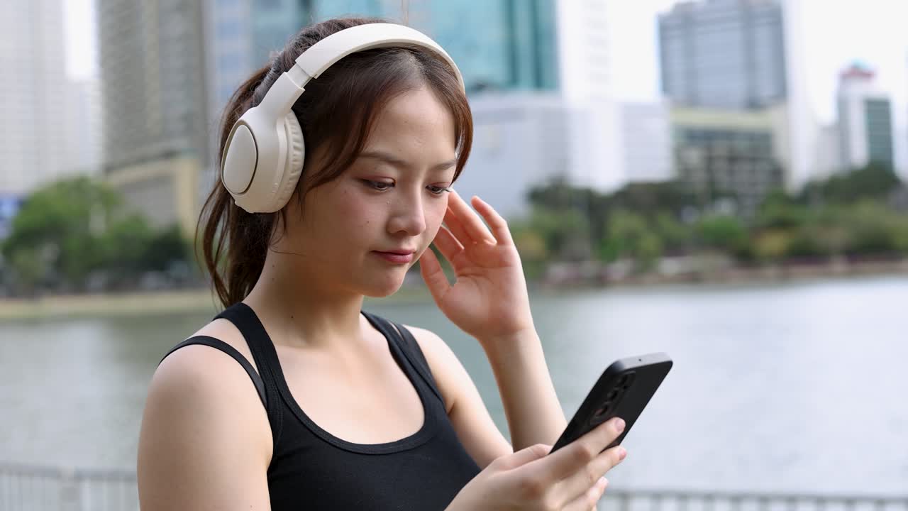 Una giovane donna con le cuffie usa il suo smartphone mentre si trova in un parco cittadino