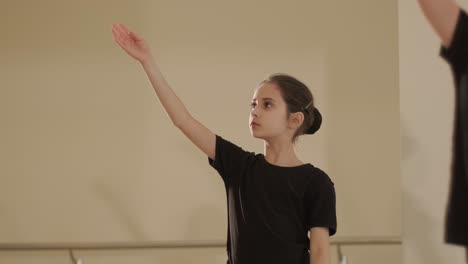 a group of young ballet students in black dancewear practicing positions in a spacious ballet studio with wooden flooring and wall-mounted barres. focused expressions and synchronized movements.