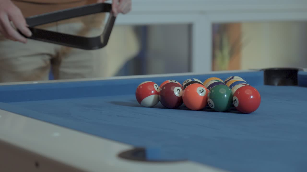 Close-ups of the hands of a man placing the billiard balls with the triangle that holds the balls to put them away before breaking the game with the cue