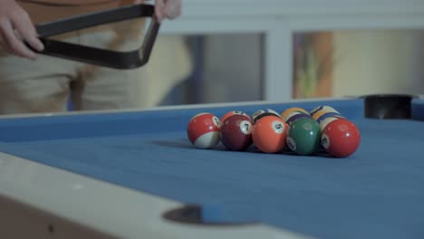 close-ups of the hands of a man placing the billiard balls with the triangle that holds the balls to put them away before breaking the game with the cue