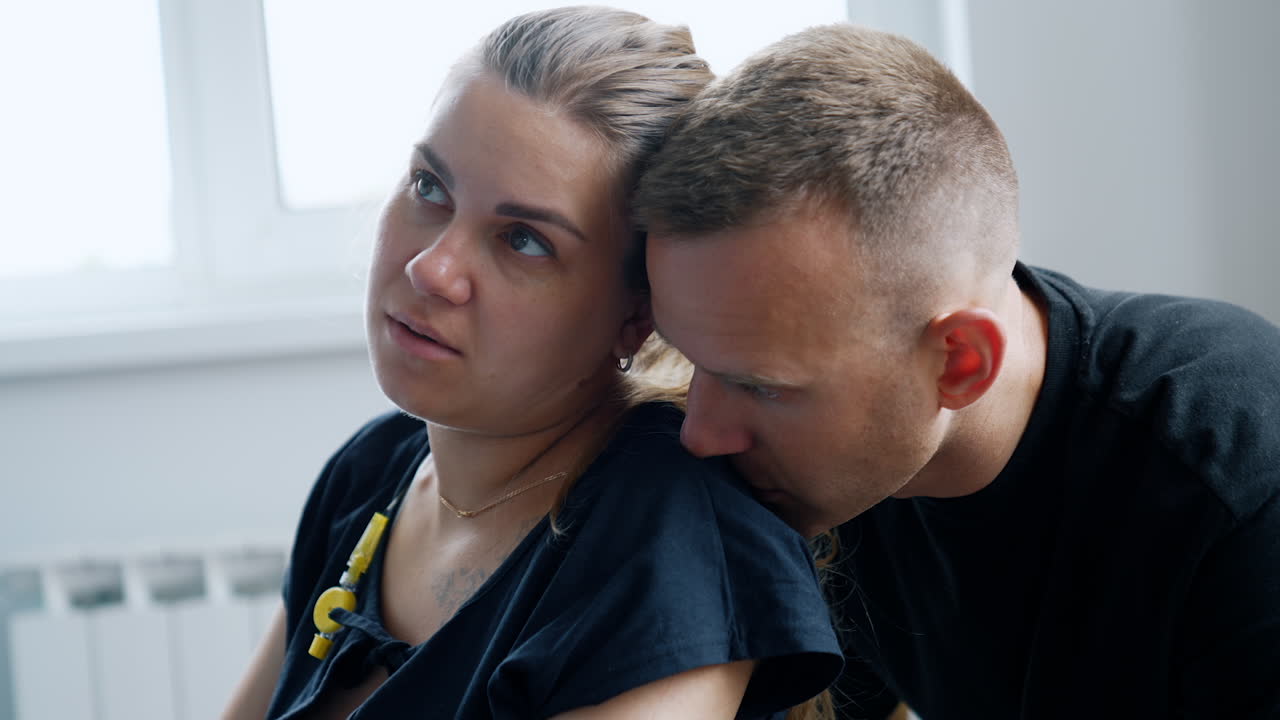 Child delivery process. Woman sits calm during the break between contractions. Husband sits behind kissing her on the shoulder. Close up.