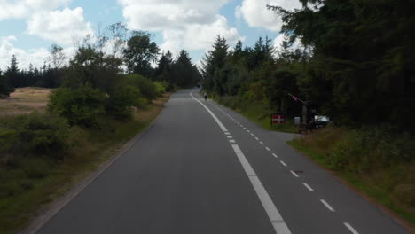 Tiefflug-über-Straße,-Vorbeifahrender-Radfahrer-Auf-Radweg.-Aufsteigende-Und-Aufschlussreiche-Bewaldete-Flachlandschaft.-Dänemark