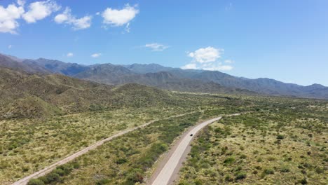 Single-vehicle-traveling-along-lonely-road-in-desert-valley-with-blue-sky