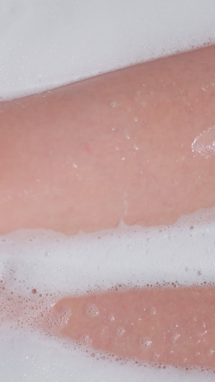 Woman bare legs in foamy water in bathtub. Slim lady takes cozy warm bath with soap froth at home. Elegant woman relaxes sitting in hot bath